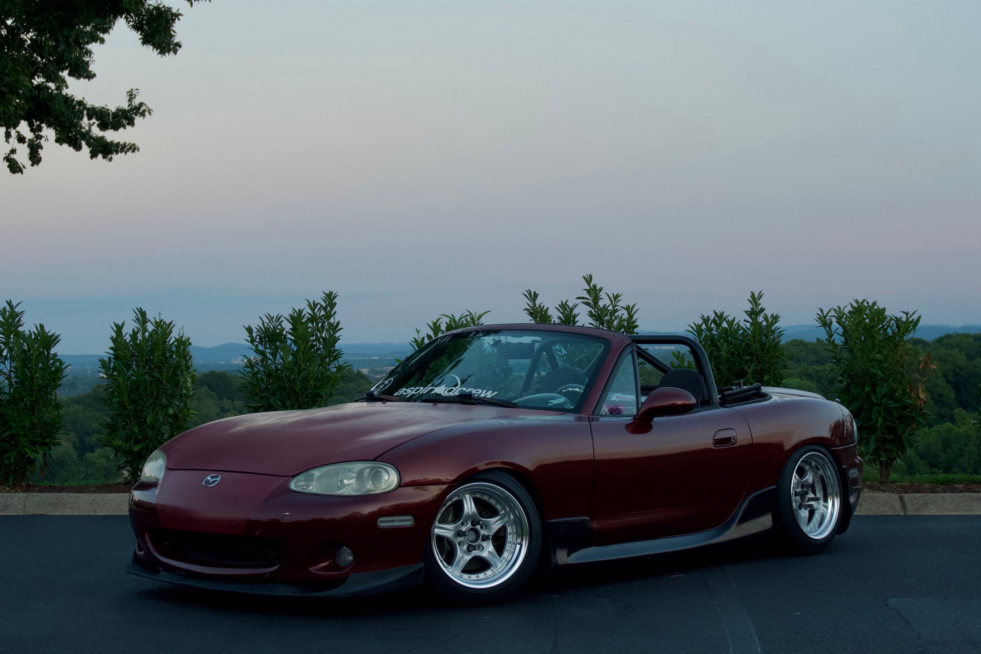 AI-generated sample: a silver NB2 Miata parked at a wooded overlook in late-afternoon light
