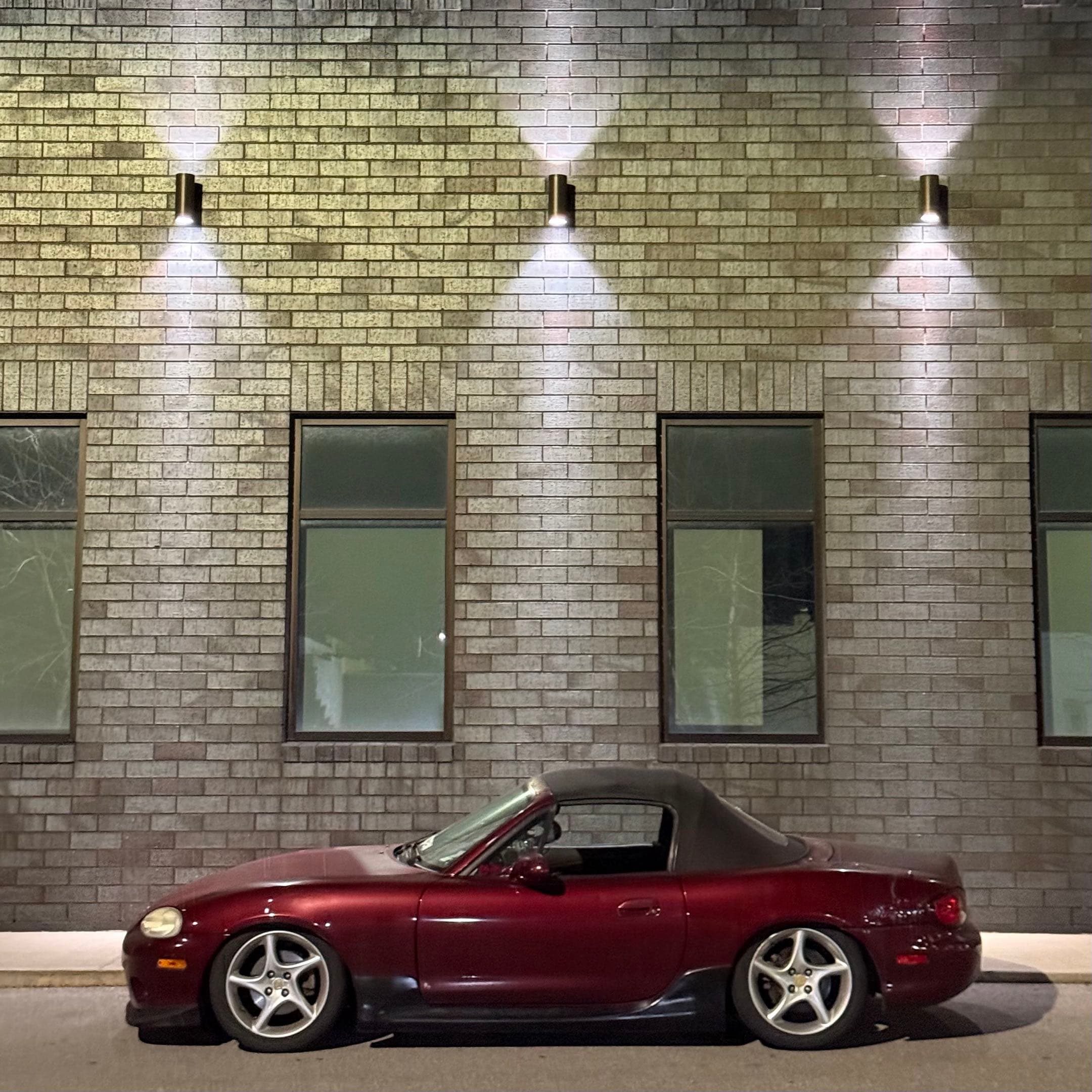 first iterated version of the miata. on stock wheels, in front of a nice well lit siding of a building.