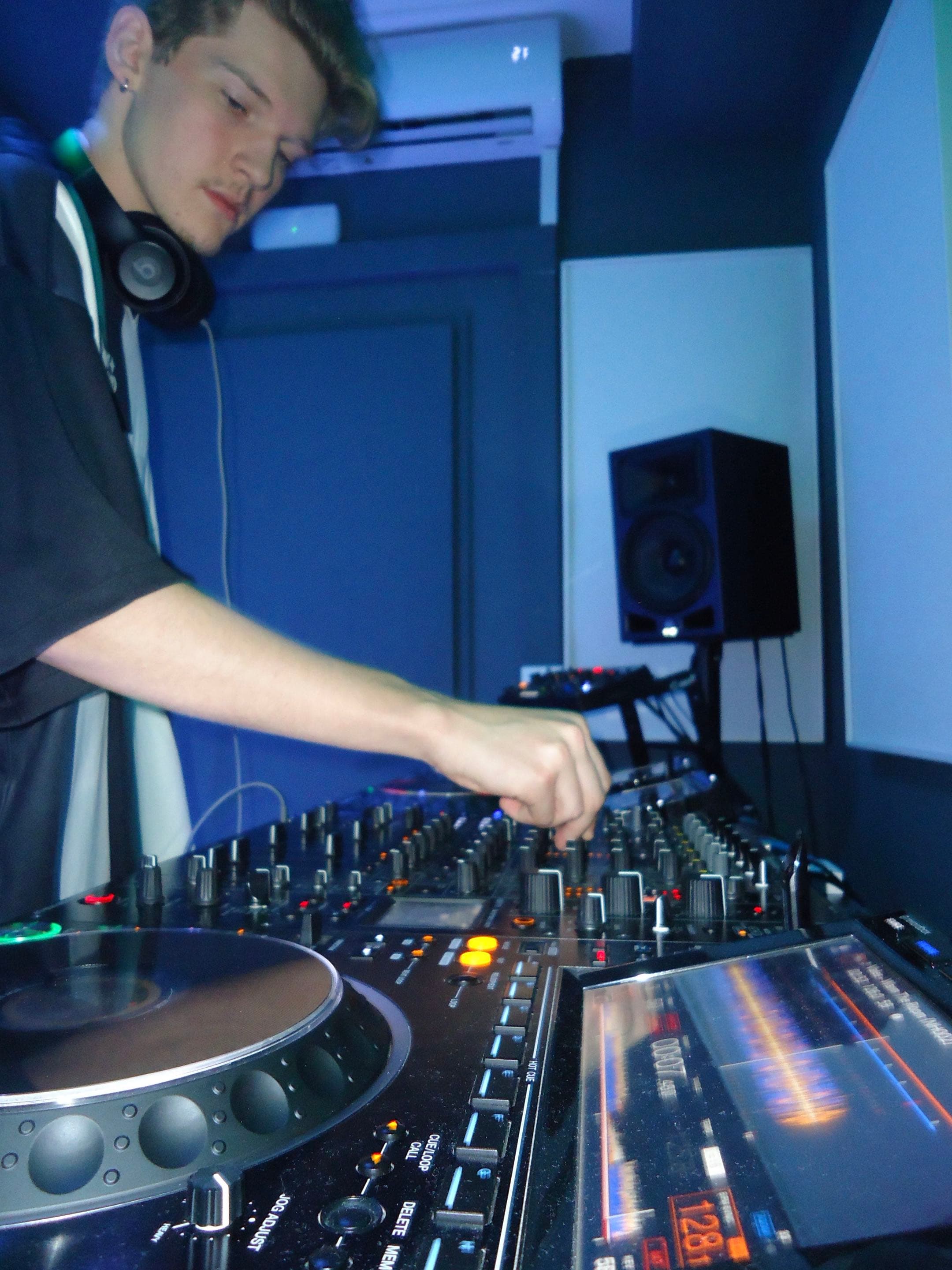 DJ adjusting a mixer beside the decks under blue lighting